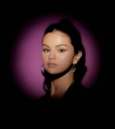 a woman with large hoop earrings on her head in front of a purple background, looking at the camera