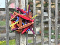 a colorful sculpture made out of wood sticks on a wooden fence post in front of a garden