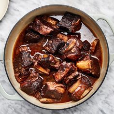 a pot filled with meat and sauce on top of a marble countertop next to a wooden spoon