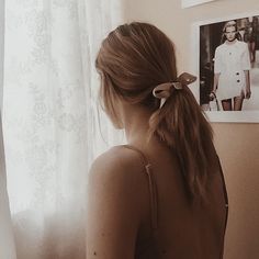 a woman standing in front of a window with her back turned to the camera and wearing a ponytail