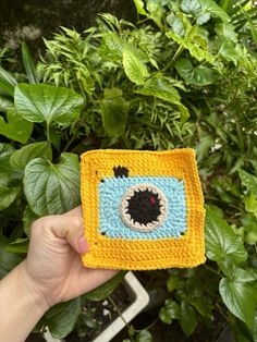 someone is holding up a crocheted square with a monster face in the center