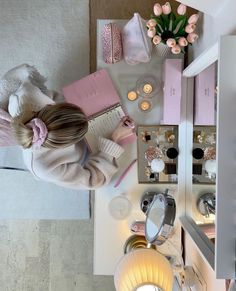 a woman sitting on top of a bed next to a table filled with makeup and other items