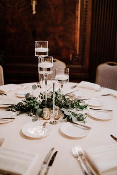 the table is set with silverware and greenery for an elegant centerpieces