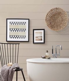 a white bath tub sitting next to a black chair and pictures on the wall above it