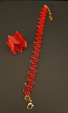 a red and gold chain with two pieces of jewelry attached to it on a black surface