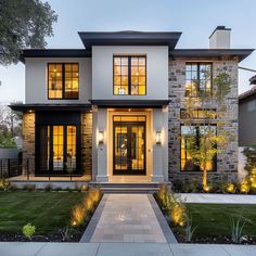 a modern house with lots of windows and lights on the front door, along with green grass