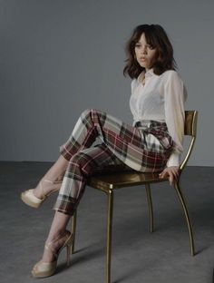 a woman sitting on top of a wooden chair wearing plaid pants and white shirt with high heels