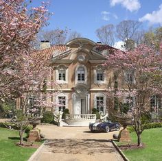 a car parked in front of a large house with pink flowers on it's trees