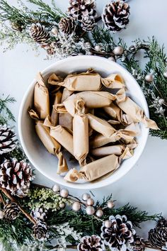 a white bowl filled with rolled up pastry next to pine cones and christmas decorations on the table