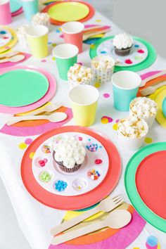 the table is set with colorful paper plates and cupcakes