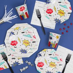 a table set with comic themed paper plates and napkins, silverware and forks