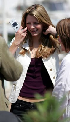 a woman holding up her cell phone to her ear while another woman looks at it