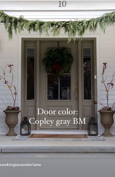 the front door is decorated for christmas with wreaths and potted plants on either side