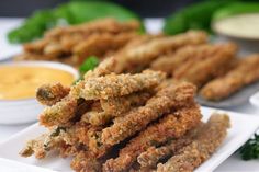 fried food items displayed on white plate with dipping sauces in bowls behind them and green leafy greens