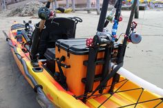 an orange and yellow kayak with fishing gear on the front is sitting in the sand