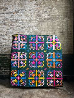 a multicolored quilt sitting on top of a wooden floor next to a brick wall