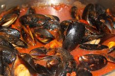 a pan filled with mussels and sauce on top of a stove