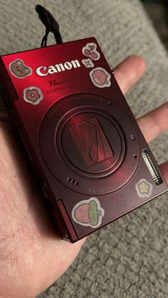 a hand holding a small red camera in it's left hand, with buttons on the front