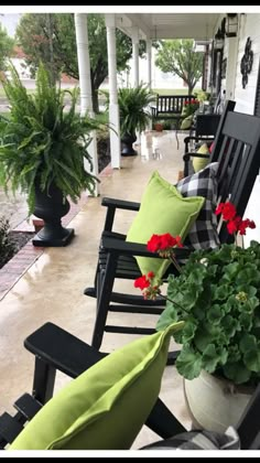 black rocking chairs with green and red pillows on the porch next to potted plants