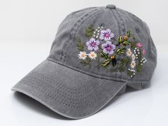 a gray baseball cap with flowers embroidered on the front and back side, sitting on a white surface