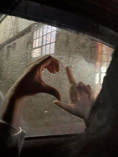 two hands reaching out the window to touch each other with their fingers in the rain