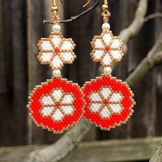 the beaded earrings are hanging on a tree branch in front of a wooden fence