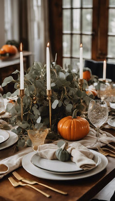 a table set with candles, plates and pumpkins