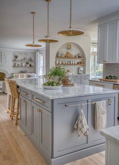 a large kitchen with an island in the center and two hanging lights above it, along with wooden flooring