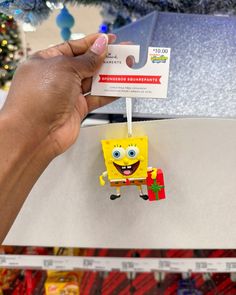 someone holding up a spongebob ornament in front of a christmas tree