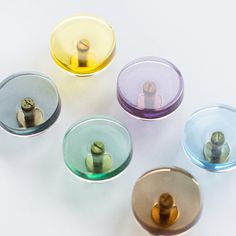 four glass bowls with different colored lids on white table top next to each other and one person standing in the middle