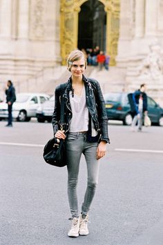 a woman standing in front of a building wearing grey jeans and a black leather jacket