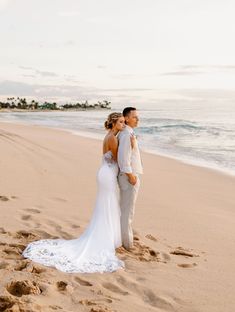 a bride and groom standing on the beach