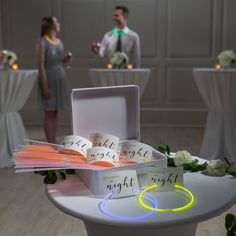 two people are standing in the background behind a table with white linens and flowers