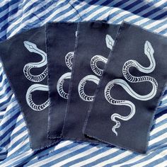 three cloth coasters with white snakes on them sitting on a blue and white striped shirt