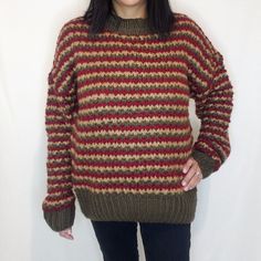 a woman standing in front of a white wall wearing a red and brown striped sweater