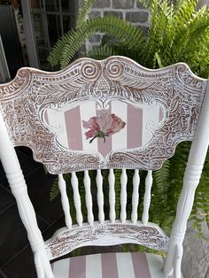 a white wooden chair with pink and white striped upholstered seat next to ferns