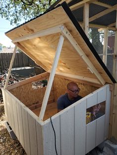 a man standing inside of a chicken coop on top of a pile of dirt next to a tree