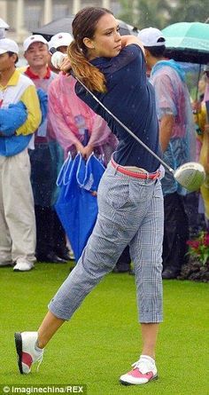 a woman swinging a golf club at a ball on the green field with people watching