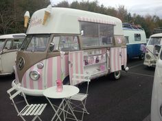 an old vw bus is parked in a parking lot with tables and chairs around it