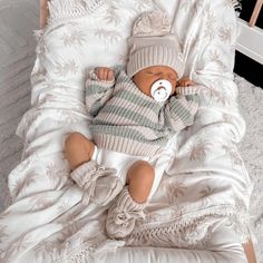 a baby laying in a crib wearing a knitted hat and sweater with a pacifier