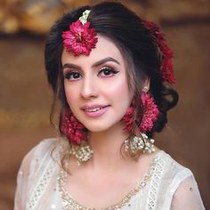 a woman with red flowers in her hair and makeup looks at the camera while smiling