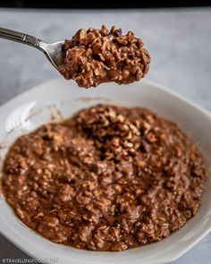 a spoonful of chocolate oatmeal with walnuts on top in a white bowl