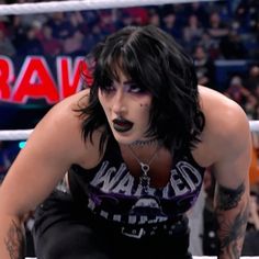 a woman with black makeup and piercings on her face sitting in a wrestling ring