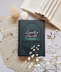 an open book sitting on top of a table next to some white flowers and candles