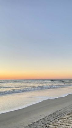 an empty beach with waves coming in to shore and the sun setting on the horizon