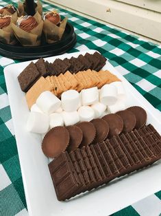 a plate with marshmallows, chocolate and cookies on it sitting on a checkered tablecloth