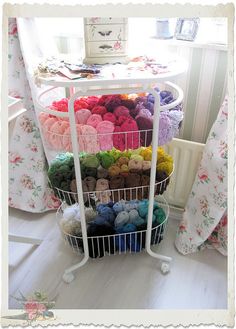 a white wire basket filled with yarn on top of a table next to a window