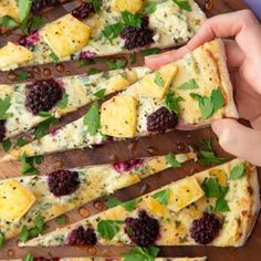 someone is holding up a piece of flat bread with cheese and berries on it while another slice has been cut in half