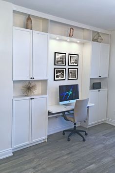 a desk with a computer on top of it in front of some white cupboards