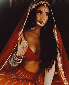 a woman in a red outfit with jewelry on her face and chest is posing for the camera